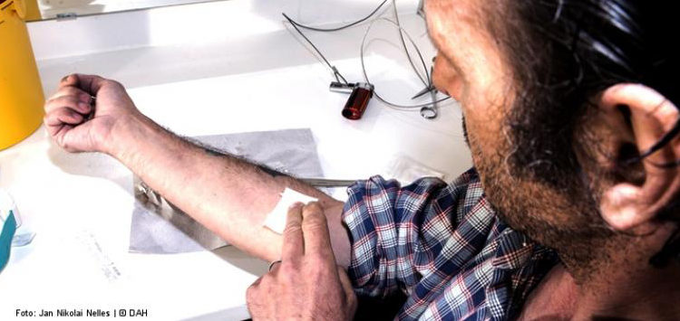 Mann drückt Tupfer auf Armbeuge