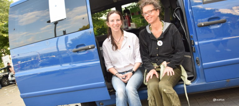 Zwei Beraterinnen sitzen vor dem blauen Bus des Projektes