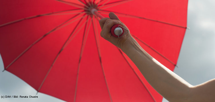 Ein Arm hält einen roten Regenschirm in die Höhe