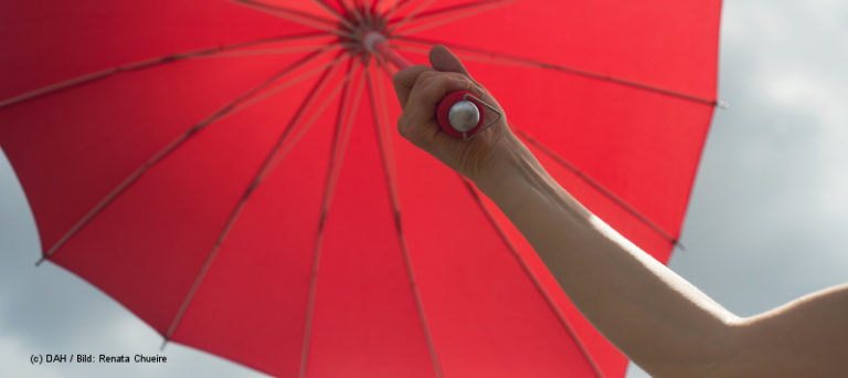 Ein Arm hält einen roten Regenschirm in die Höhe