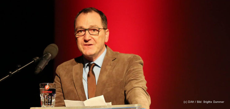 Das Bild zeigt DAH-Vorstandsmitglied Manuel Izdebski, der sich im Interview gegen Rechtspopulismus positioniert, hinter einem Rednerpult