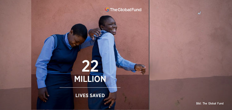 Zwei lachende Mädchen in Schuluniform stehen vor einer braunen Wand, davor der Text "22 million lives saved", oben das Logo des Global Fund.