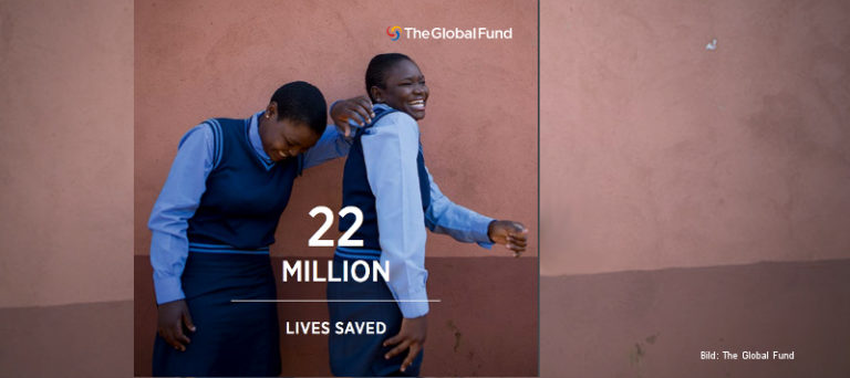 Zwei lachende Mädchen in Schuluniform stehen vor einer braunen Wand, davor der Text "22 million lives saved", oben das Logo des Global Fund.