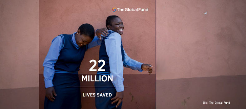 Zwei lachende Mädchen in Schuluniform stehen vor einer braunen Wand, davor der Text "22 million lives saved", oben das Logo des Global Fund.