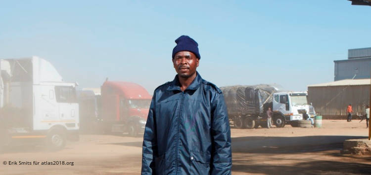 Afrikanischer Mann in blauer Jacke vor LKWs
