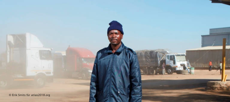 Afrikanischer Mann in blauer Jacke vor LKWs