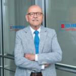 Porträt Rolf Rosenbrock vor Glastür mit dem Logo des Paritätischen Wohlfahrtsverbands