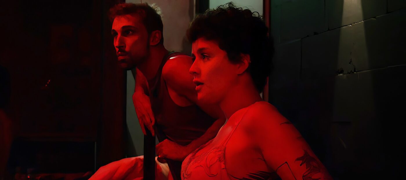 Szenenfotoeine zwei Personen im sitzen nebeneinander in einem rot beleuchteten Raum