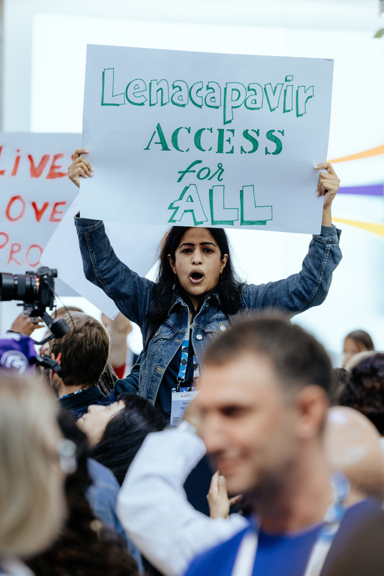 Demo auf der Welt-Aids-Konferenz 2024, Person ragt aus der Menge und hält Schild mit folgendem Text hoch: Lenacapavir ACCESS for ALL