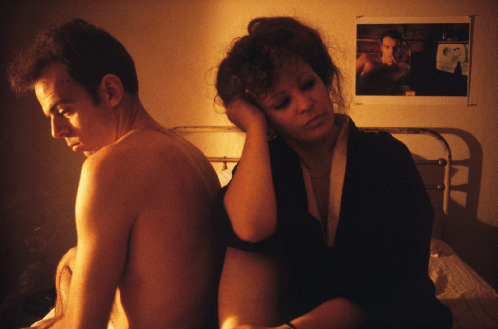 Nan Goldin im Kimono mit einer männlichen Person im Bett sitzend, an der Wand ein Foto des Mannes
