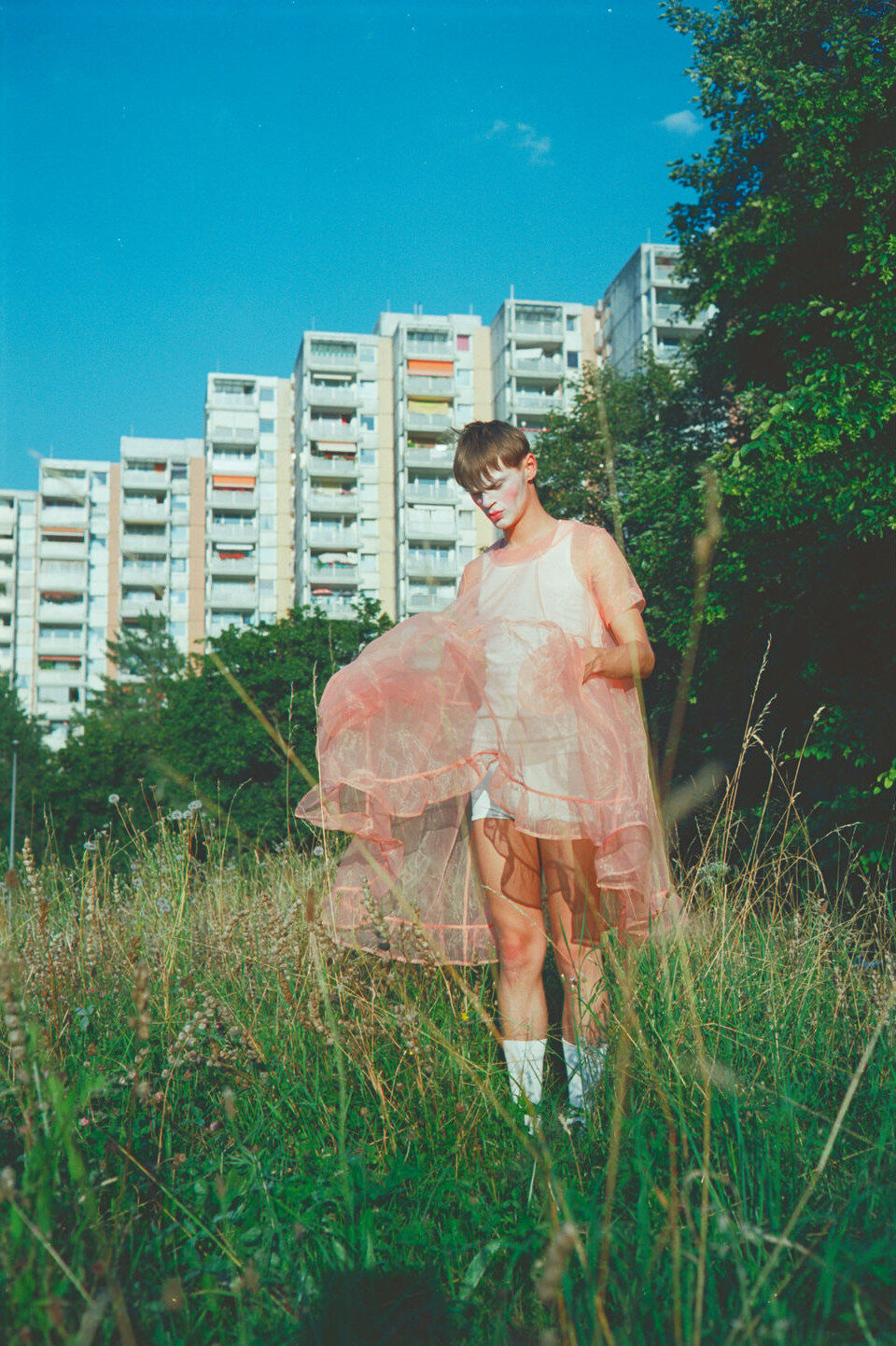 Person im rosa Tüllkleid auf einer Wiese vor Hochäusern