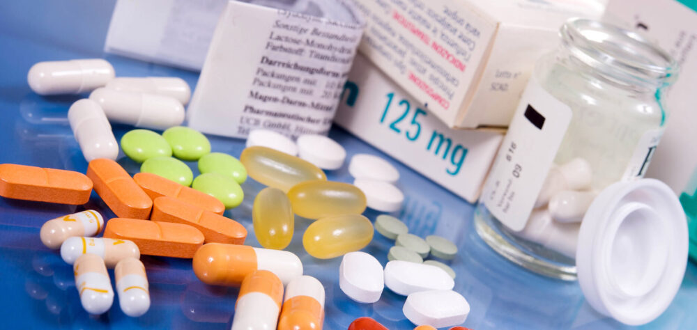 Medikamentenpackungen, Tabletten und Kapseln in verschiedenen Farben auf einer blauen Fläche