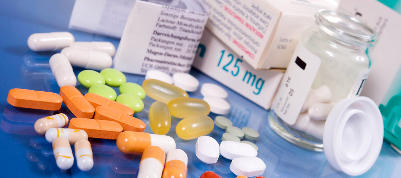 Medikamentenpackungen, Tabletten und Kapseln in verschiedenen Farben auf einer blauen Fläche