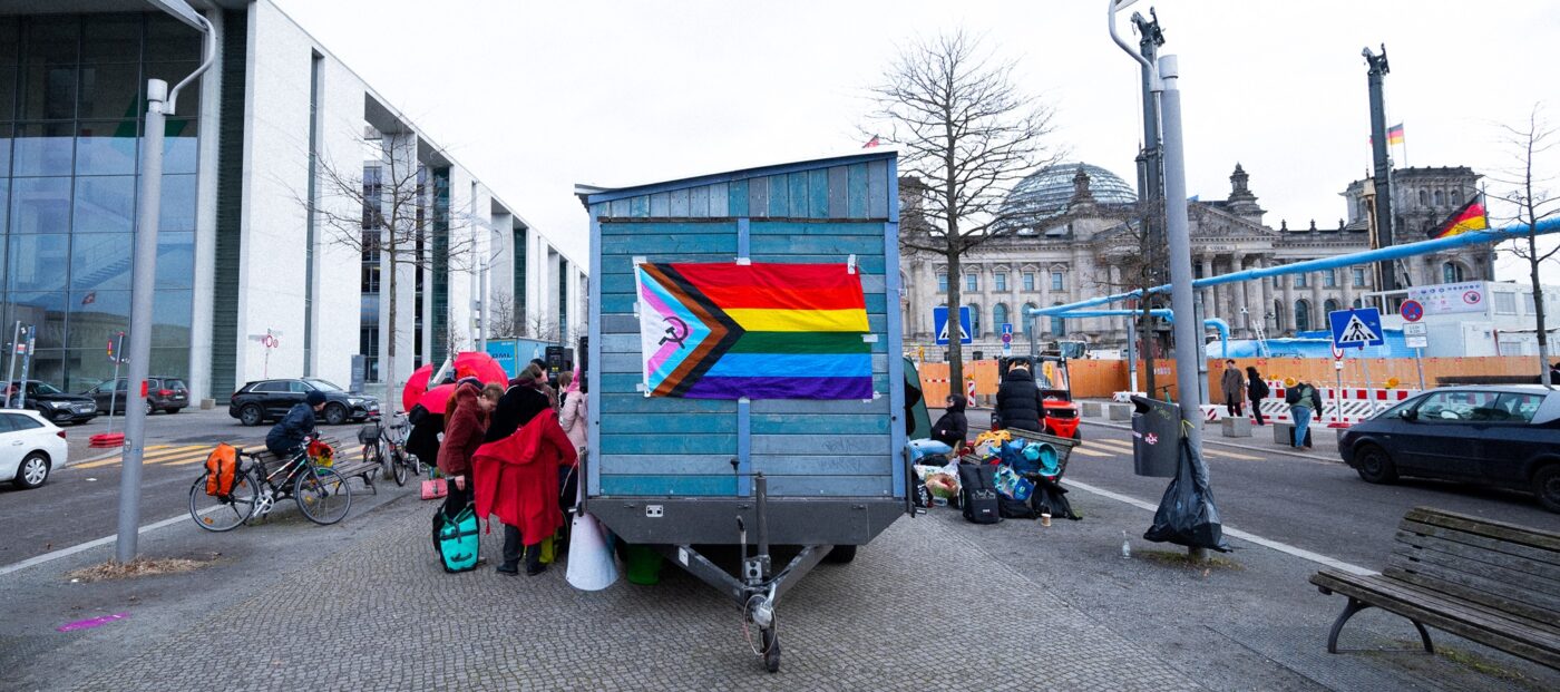 Ein Saunawagen mit Regenbogenflagge steht zwischen Paul-Löbe-Haus und Bundestag