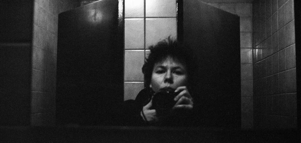 schwarz-weiß Selbstporträt in einem gekachelten Raum vor dem Spiegel