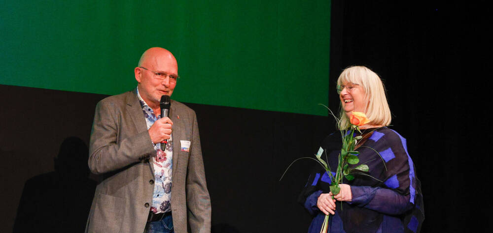 Mann mit Mikro und Frau mit Rose in der Hand stehen auf einer Bühne