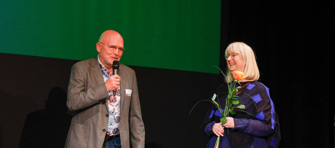 Mann mit Mikro und Frau mit Rose in der Hand stehen auf einer Bühne