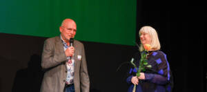Mann mit Mikro und Frau mit Rose in der Hand stehen auf einer Bühne