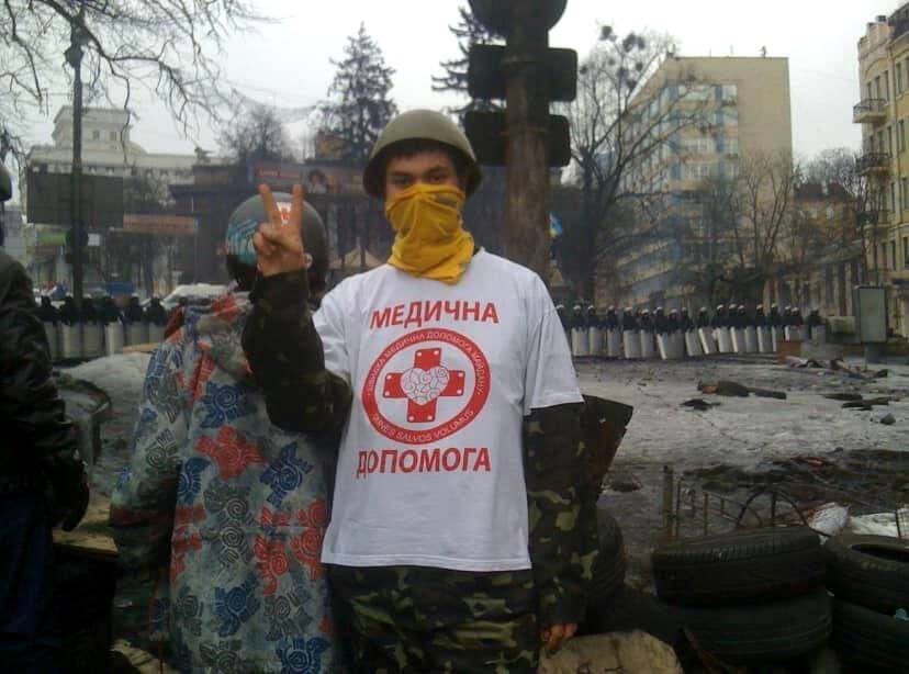 Soldat im Protestshirt mit Tuch vorm Gesicht mit Hand zum V hochgehalten