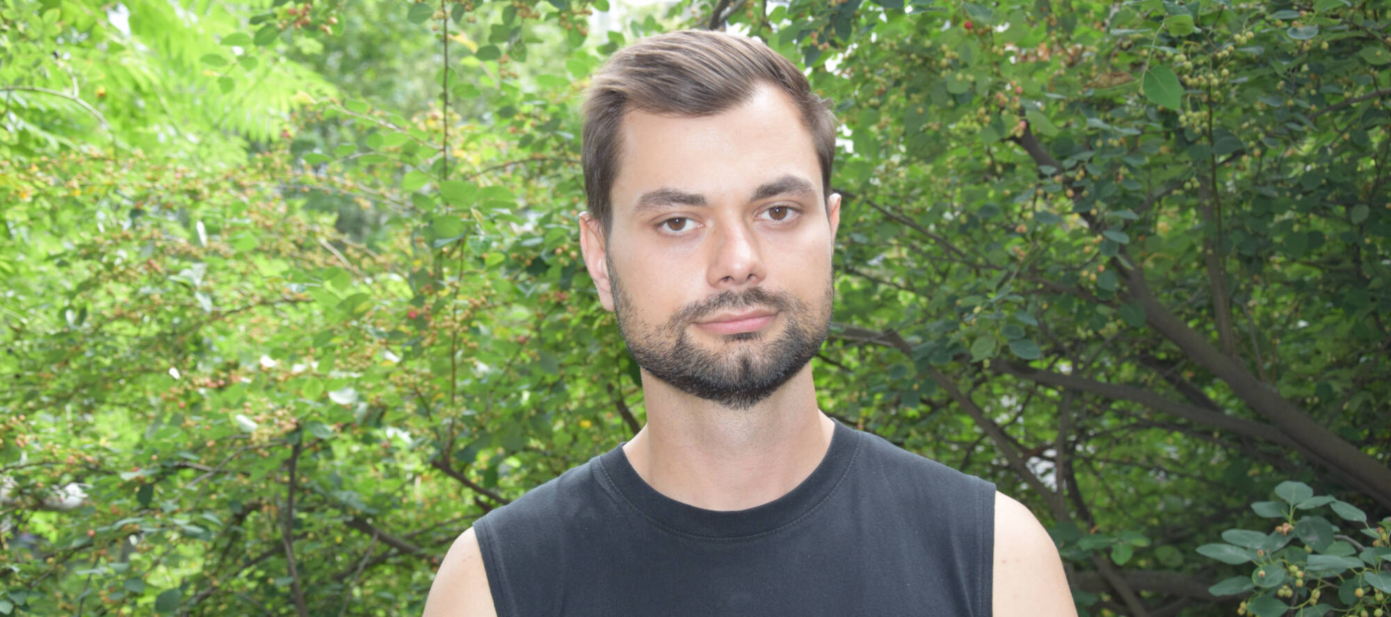 Porträt von Borys Hrachov im schwarzen Top vor grünen Bäumen