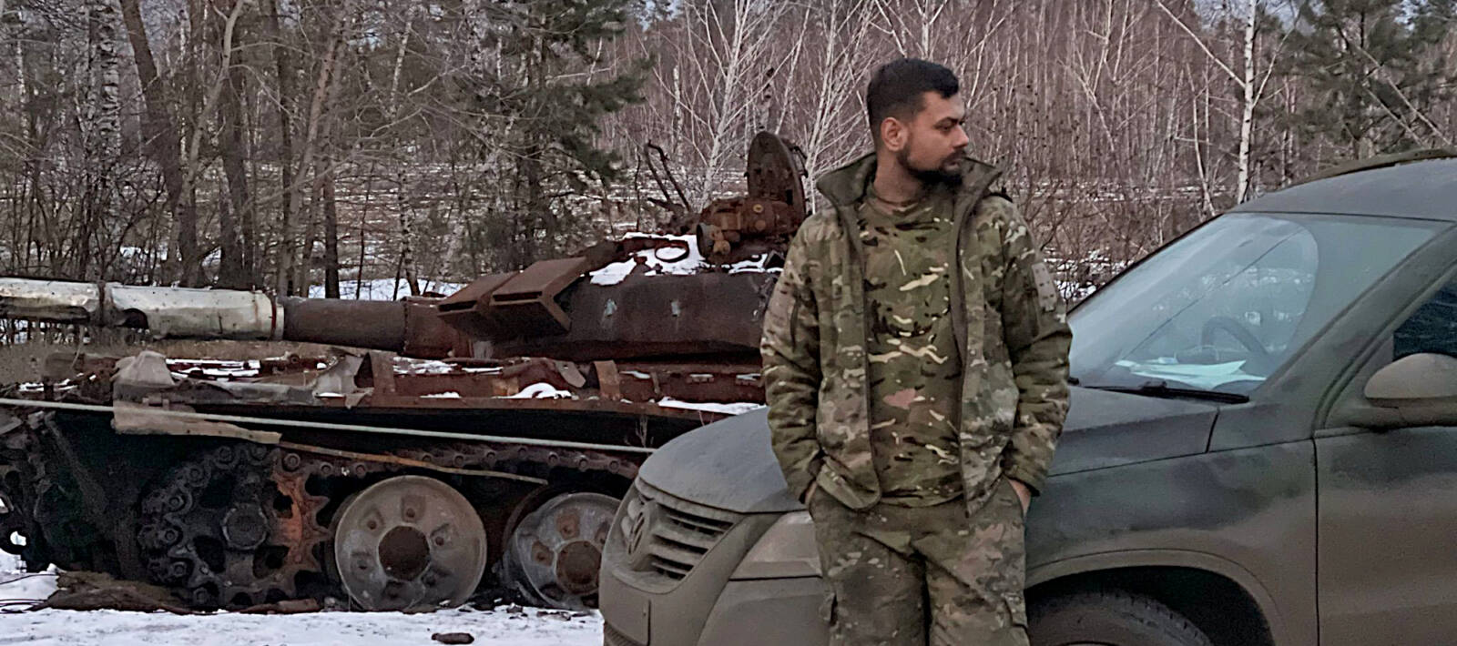 Soldat im Tarnanzug steht vor Militärfahrzeugen, es liegt Schnee
