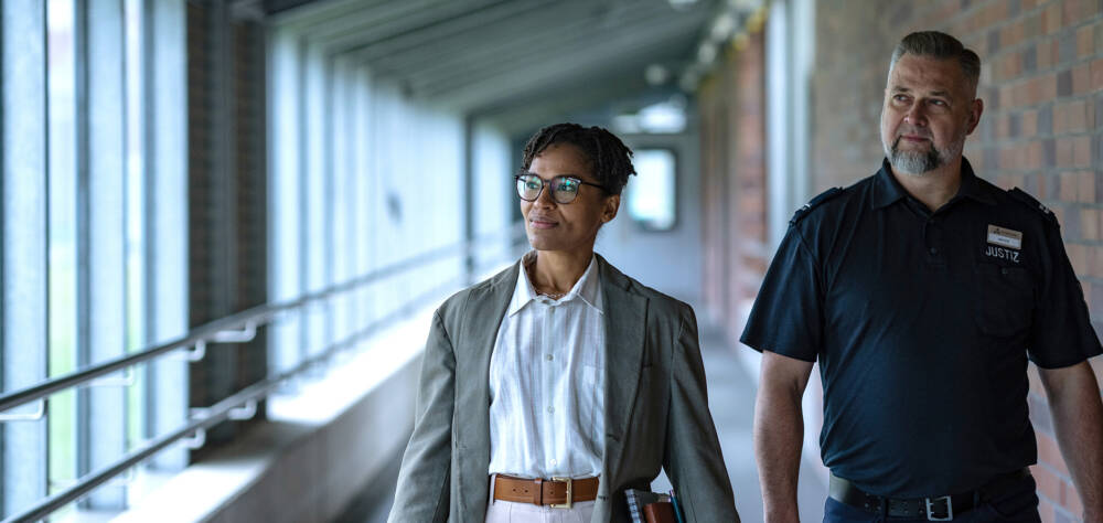 Zwei Personen gehen durch einen Flur, eine trägt ein Namensschild mit