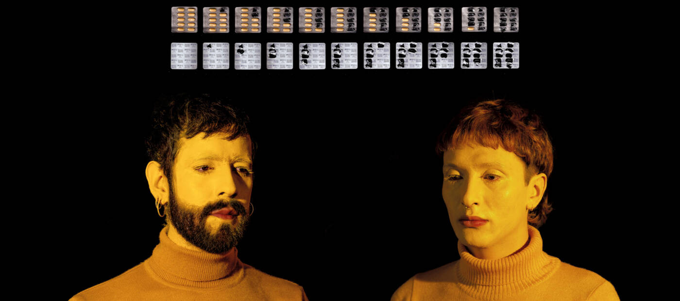 Porträt zweier Personen mit Rollkragenpullover und weiß geschminktem Gesicht, darüber zwei Reihen Pillenblister, teilweise entleert