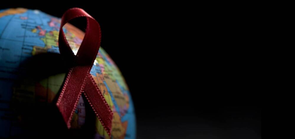 Rote Ansteckschleife auf einem Globus mit viel Schatten vor schwarzem Hintergrund.