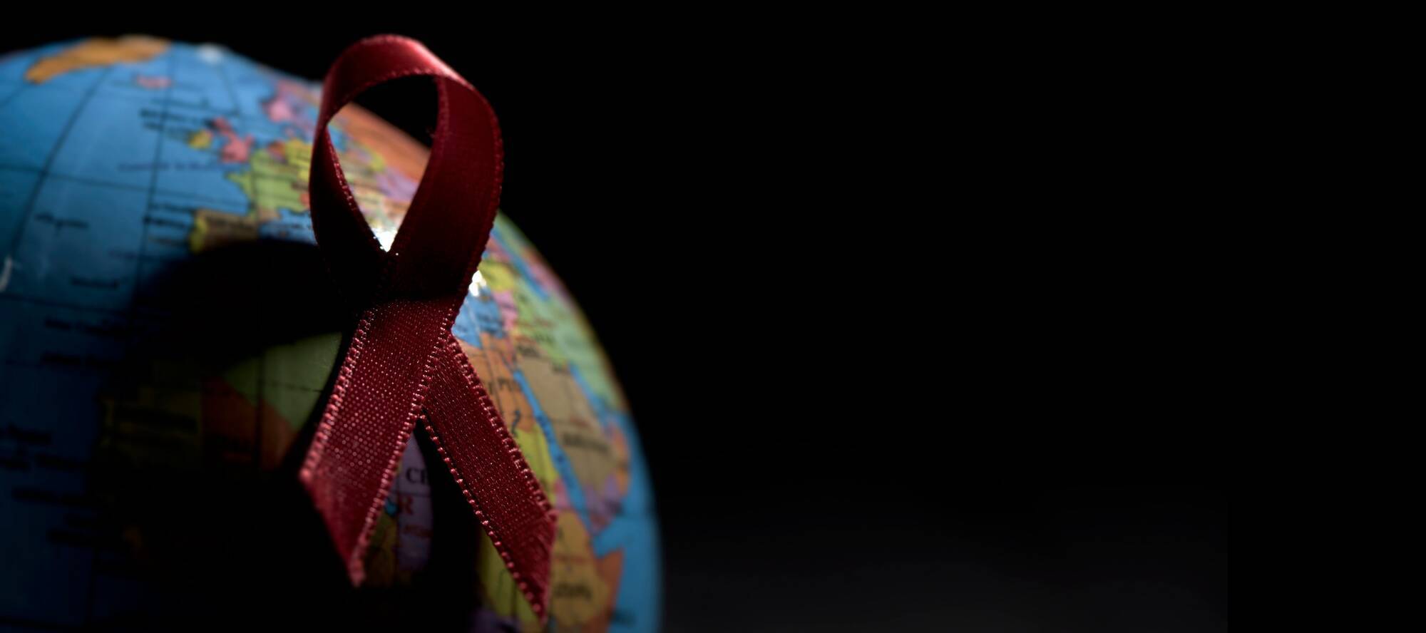 Rote Ansteckschleife auf einem Globus mit viel Schatten vor schwarzem Hintergrund.