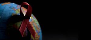 Rote Ansteckschleife auf einem Globus mit viel Schatten vor schwarzem Hintergrund.