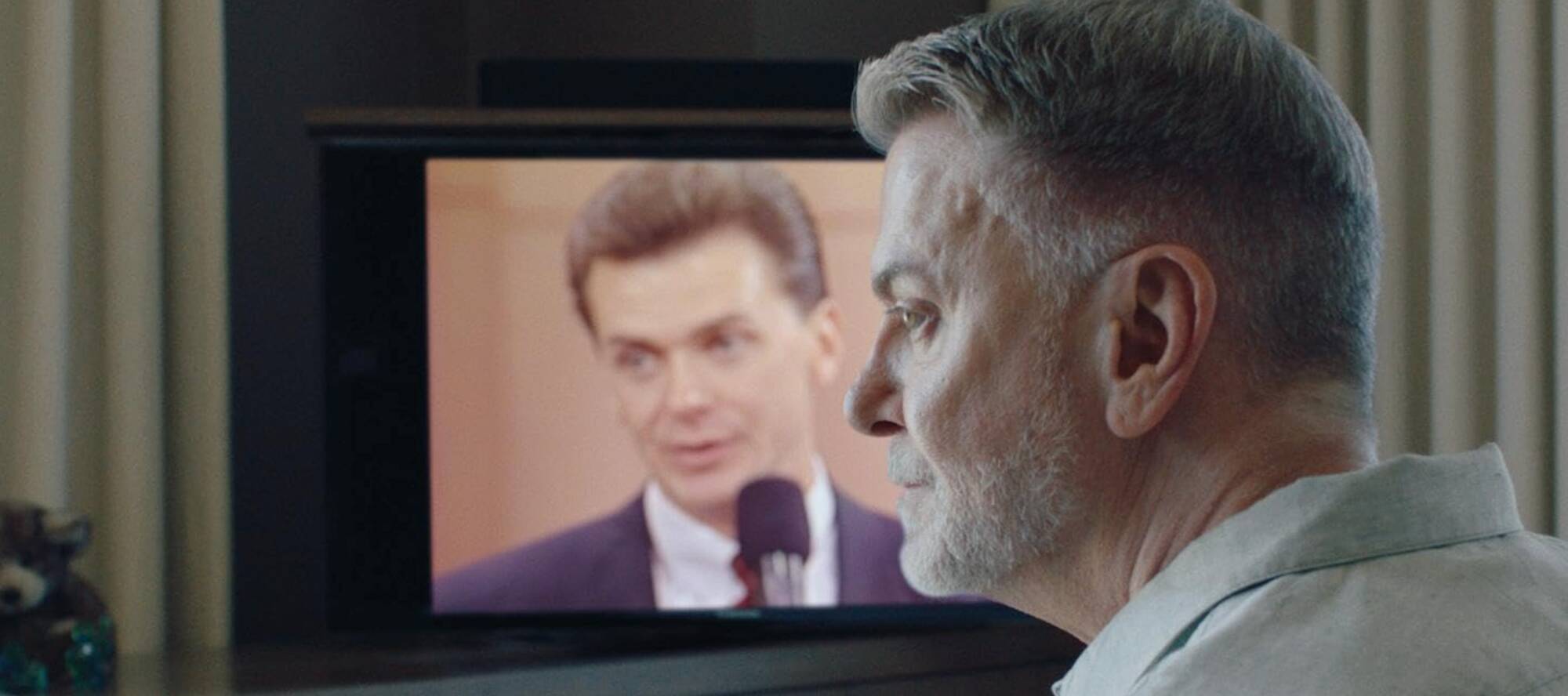 Mann im Profil vor einem Fernsehbildschirn, auf dem er in jüngeren Jahren zu erkennen ist