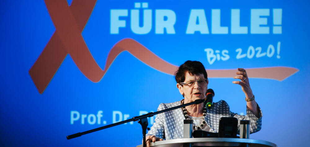 Rita Süssmuth am Redepult, Hintergrund: eine rote Aidsschleife und die Schrift 