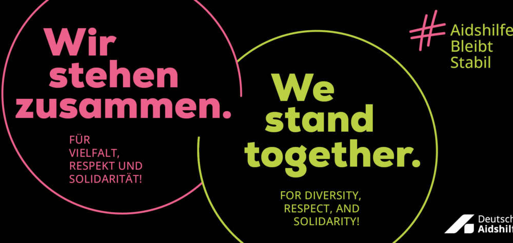 Banner mit Slogan: „Wir stehen zusammen. Für Vielfalt, Respekt und Solidarität! We stand together. For diversity, respect, and solidarity! #AidshilfeBleibtStabil, Logo Deutsche Aidshilfe