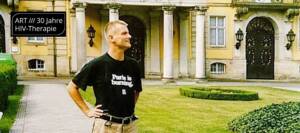 Mann in schwarzem T-Shirt mit Schriftzug "Paris is Burning" in der Einfahrt eines Herrenhauses
