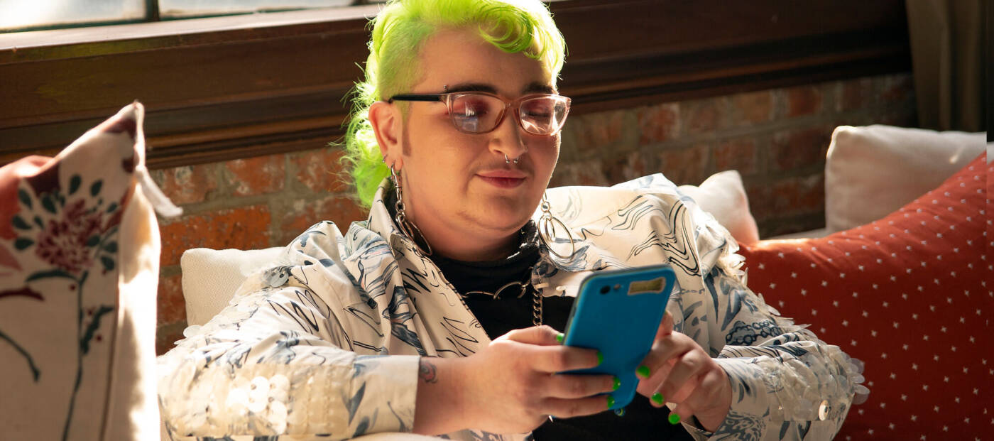 A genderqueer person looking at their phone