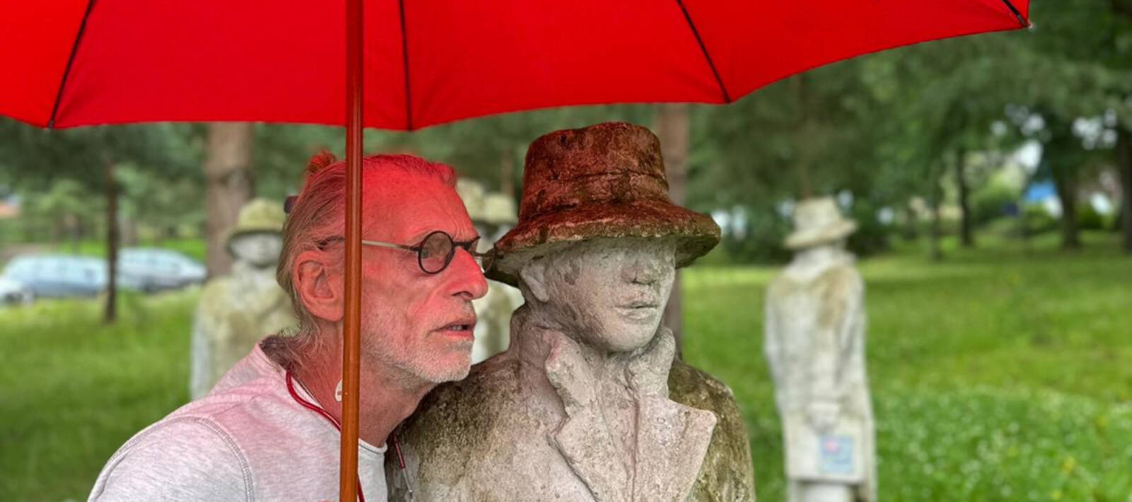 Mann mit rotem Regenschirm neben einer Steinskulptur in einem Park